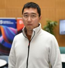 A man with tanned skin, black short hair, glasses wearing a white fleece looking at the camera.