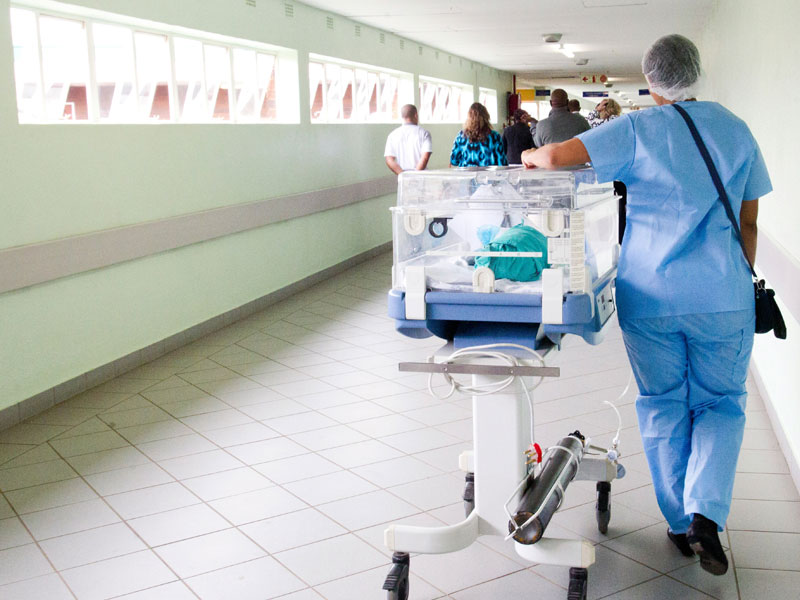 a nurse in Africa walks away from the camera with a child in an incubation unit