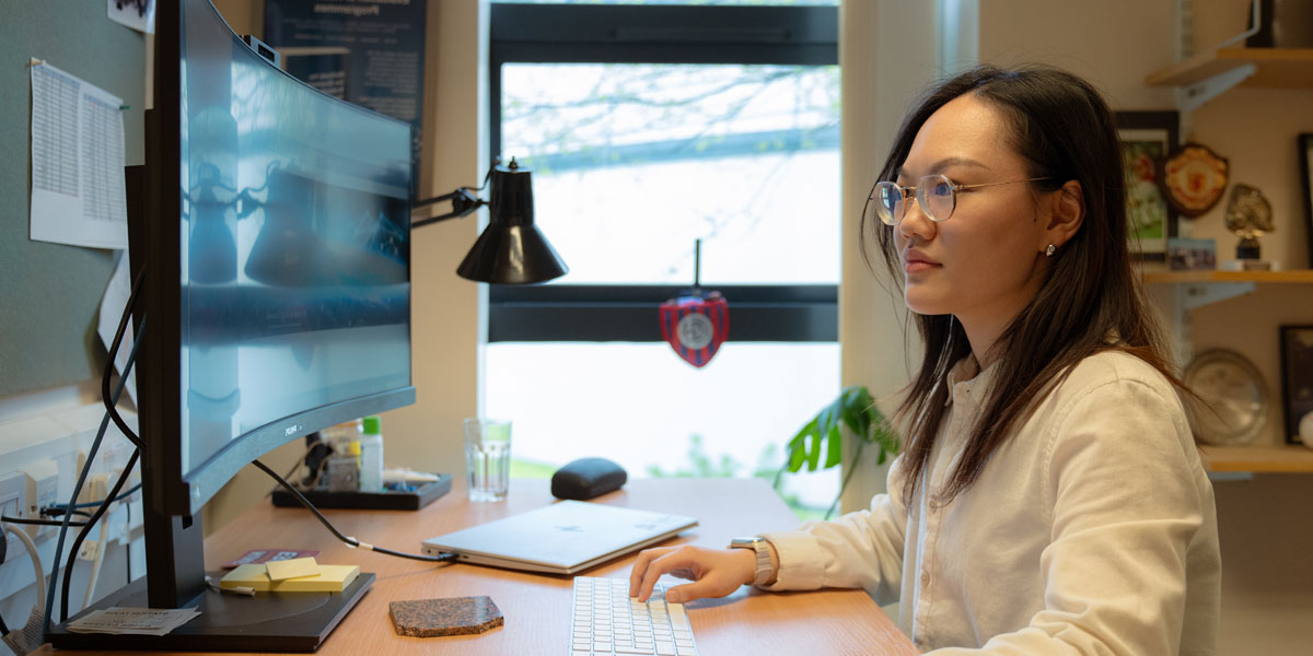 A researcher works at a computer workstation in front of a large curved screen