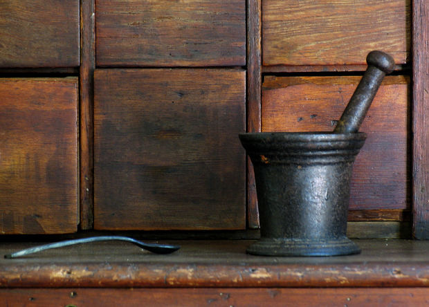 A metal pestle and mortar and spoon in front of wooden drawers