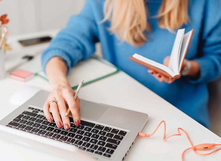 A student sits at a desk with a laptop and book