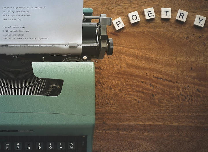 An old typewriter with Scrabble tiles next to it spelling 'poetry'