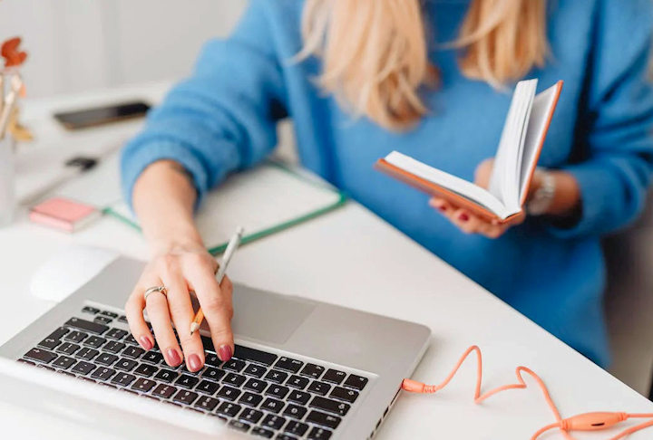 A student sits at a desk with a laptop and book