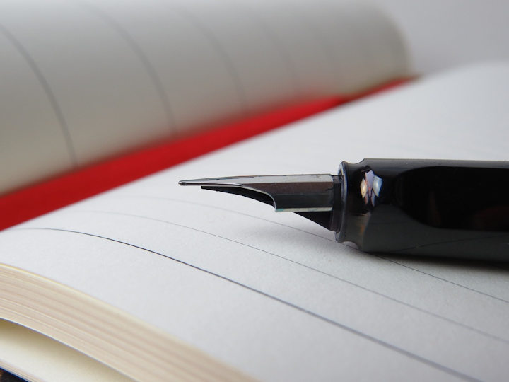 A fountain pen on a lined notebook with a red marker ribbon