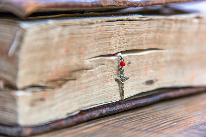 An old book with a crucifix bookmark or rosary marking a page