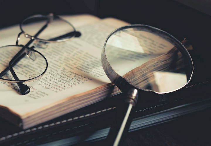 An open book with a magnifying glass and a pair of glasses