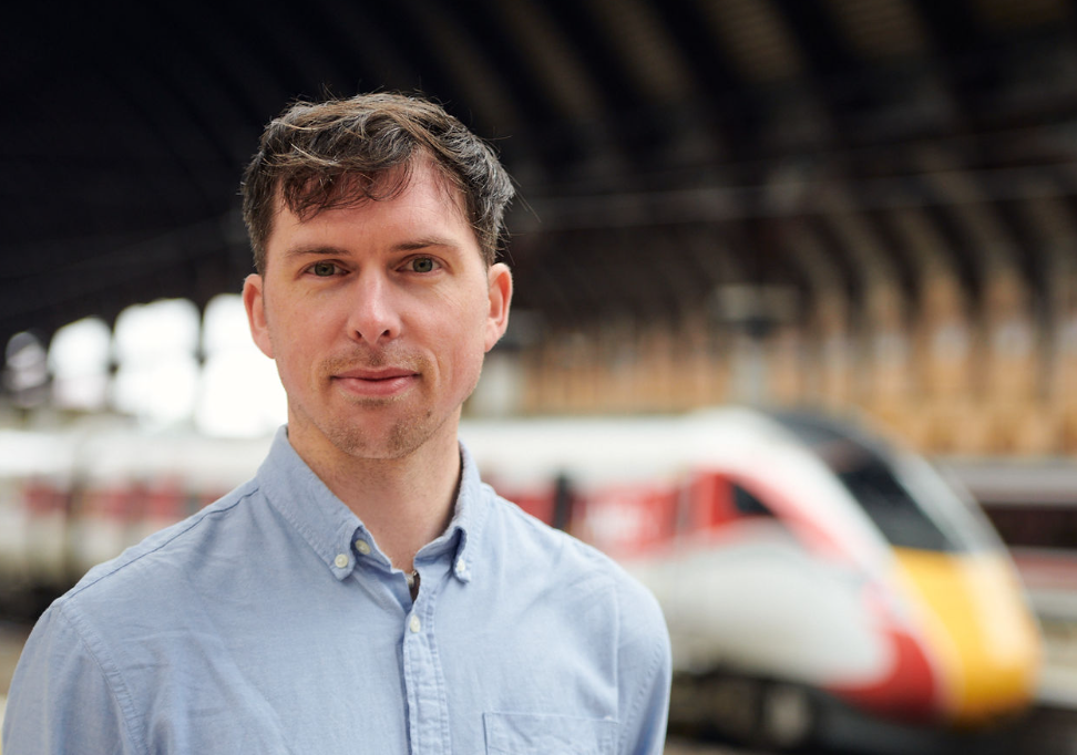 Ross Welham stood in front of an LNER train. The train is out of focus.