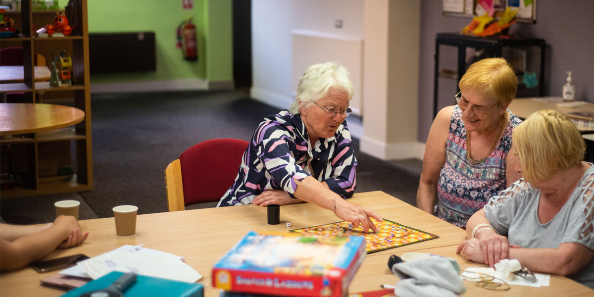 Three ladies play a board game around a table in a care facility