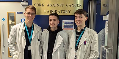 Researchers from the Jack Birch Unit who are running in the Marathon to fundraise for York Against Cancer. They're stood in front of the sign for the York Against Cancer Laboratory.