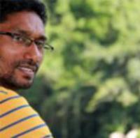 Dr Sisira Rajapakse looking over right shoulder, against a background of green foliage